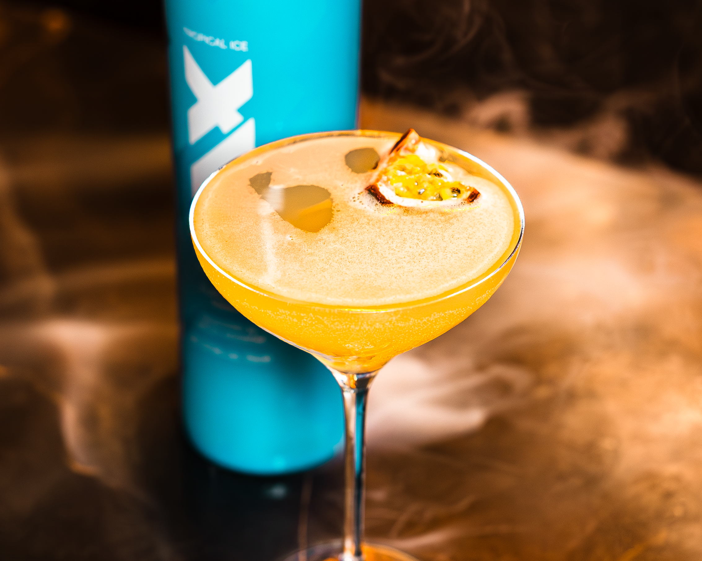 Blue bottle labeled 'XIX' next to a cocktail with a tropical twist on the pornstar martini on a reflective surface.