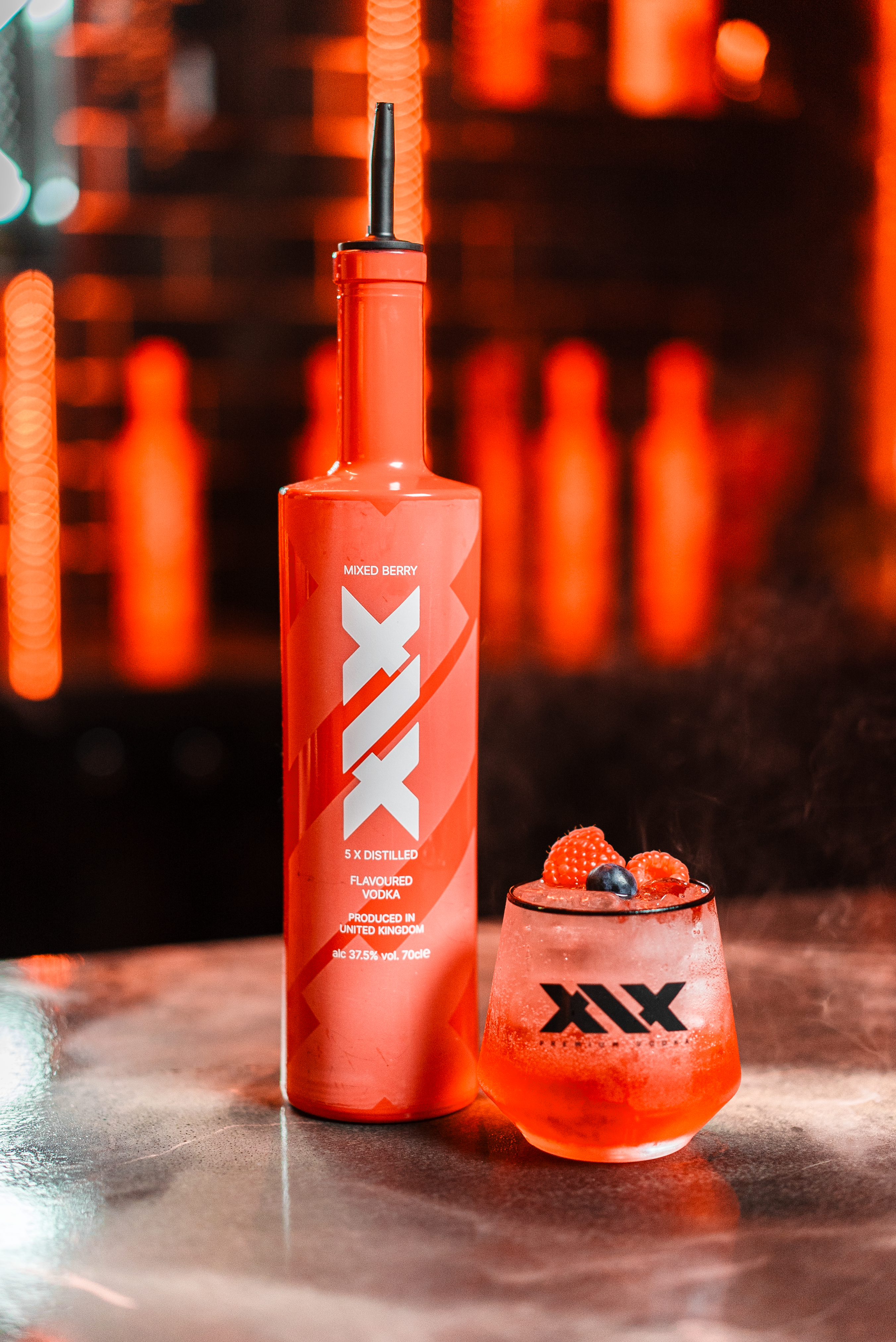 XIX bottle and cocktail with fruit garnish on a bar counter