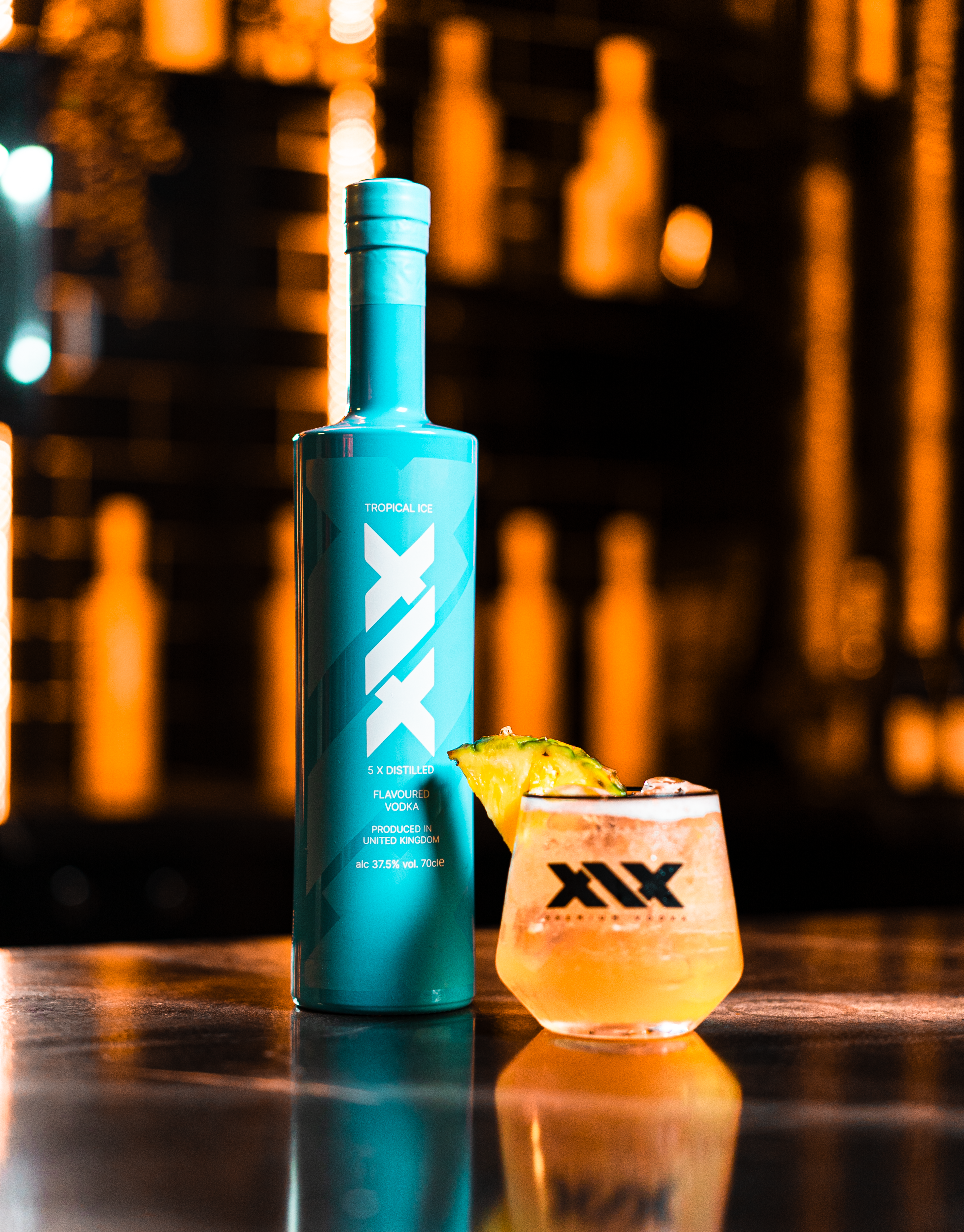 Blue bottle and glass with 'XIX' branding on a bar counter with blurred lights in the background