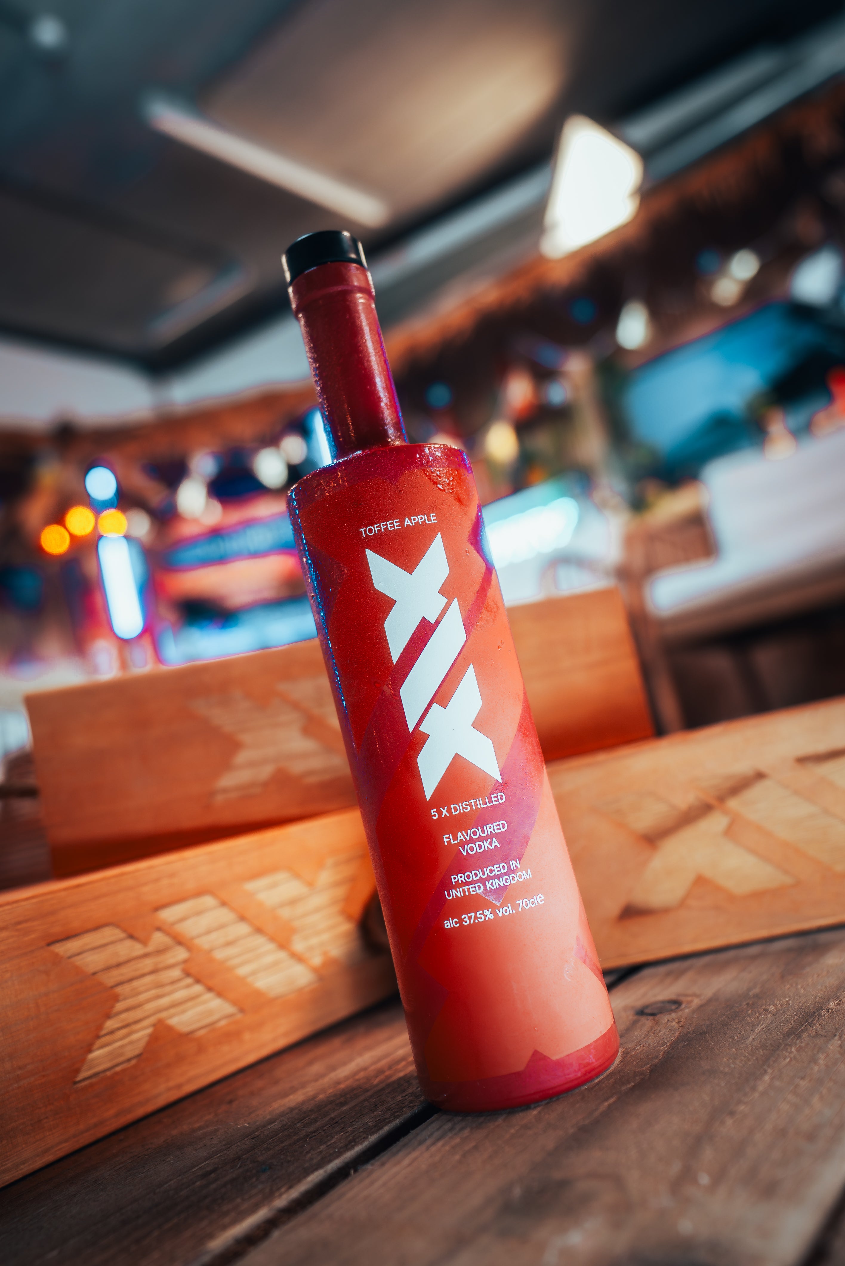 Brown bottle with white text on a wooden surface in a blurred indoor setting