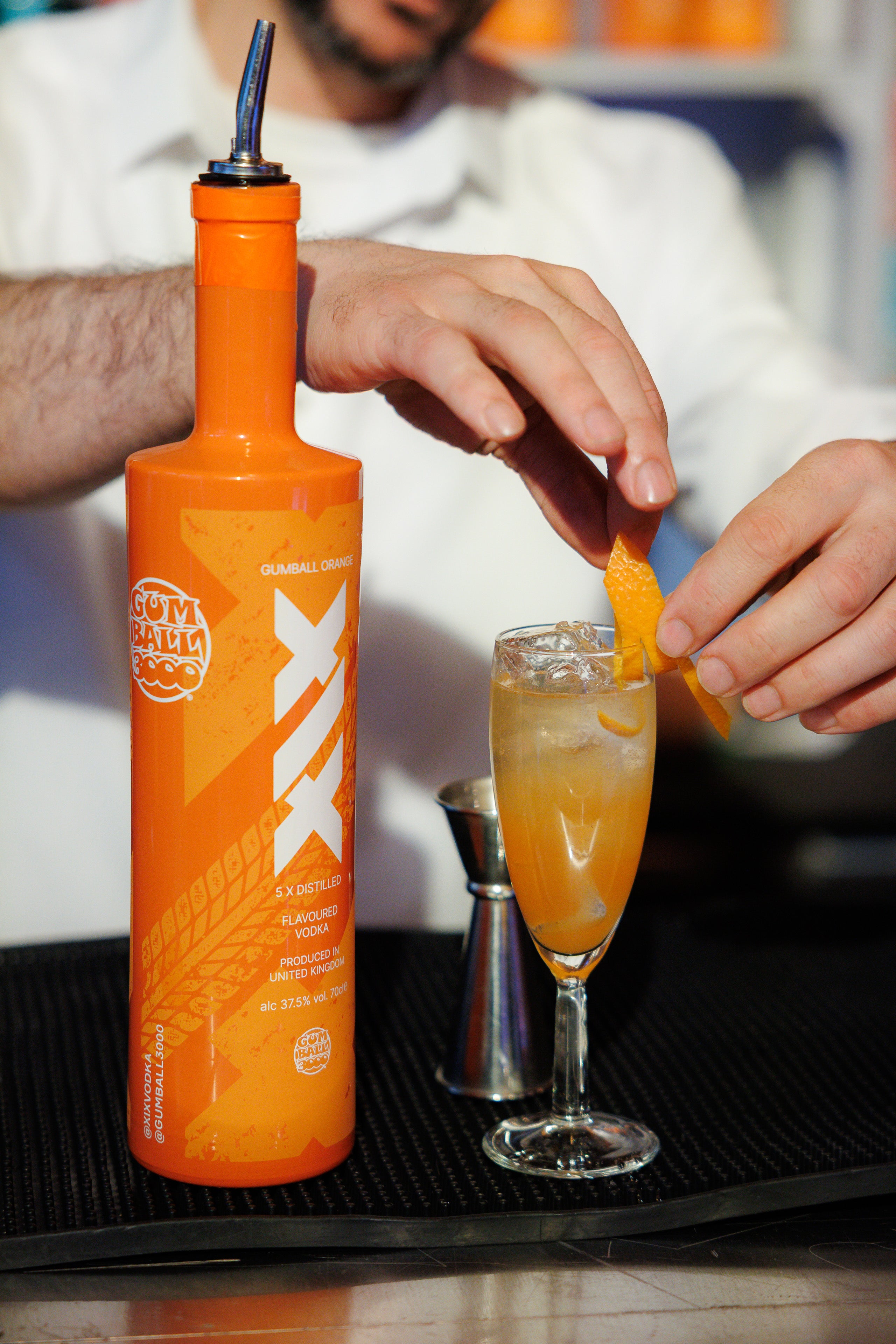 Bar tender making a drink from an orange bottle into a glass on a bar counter.