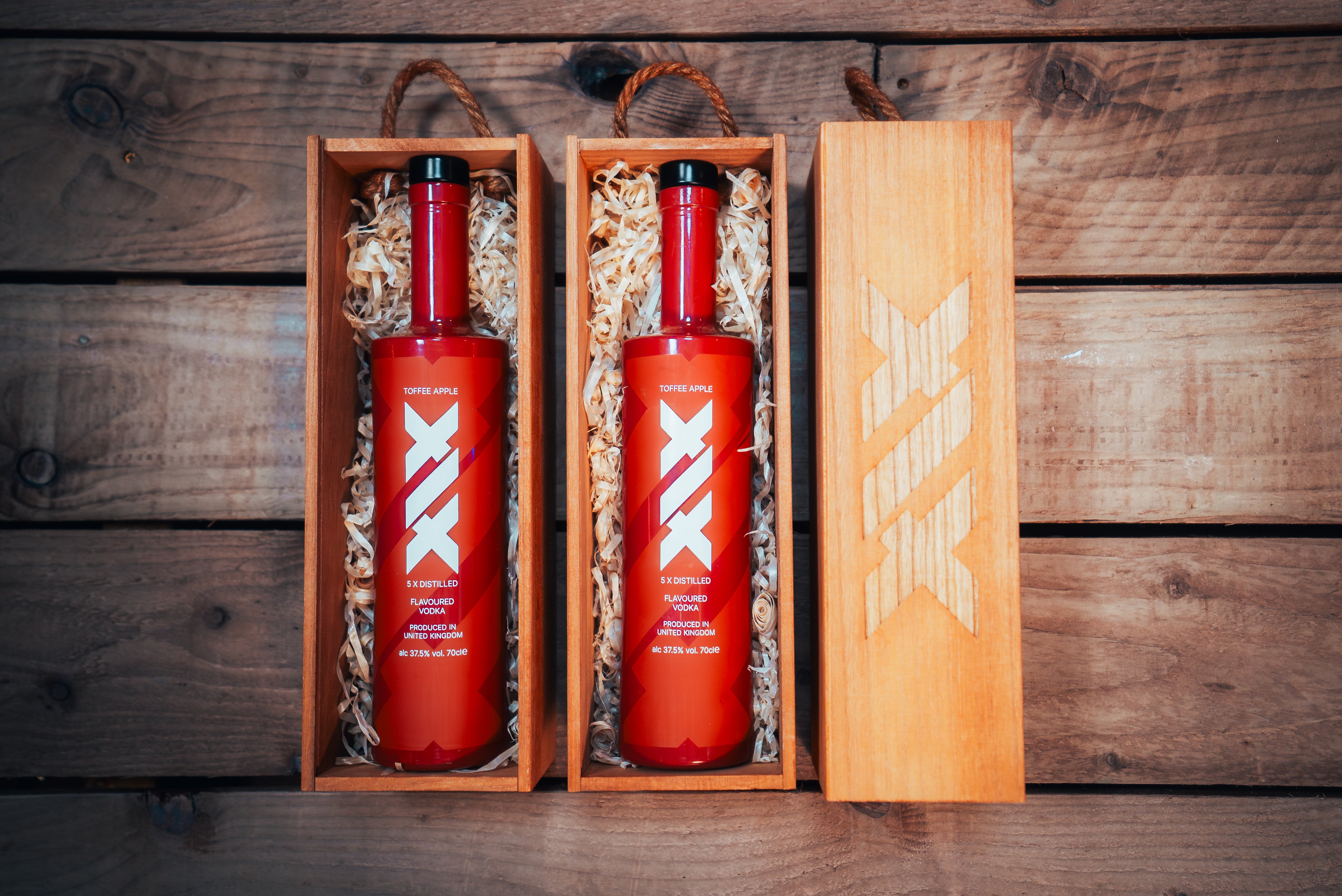 Two brown bottles with a white logo in wooden gift boxes on a wooden surface