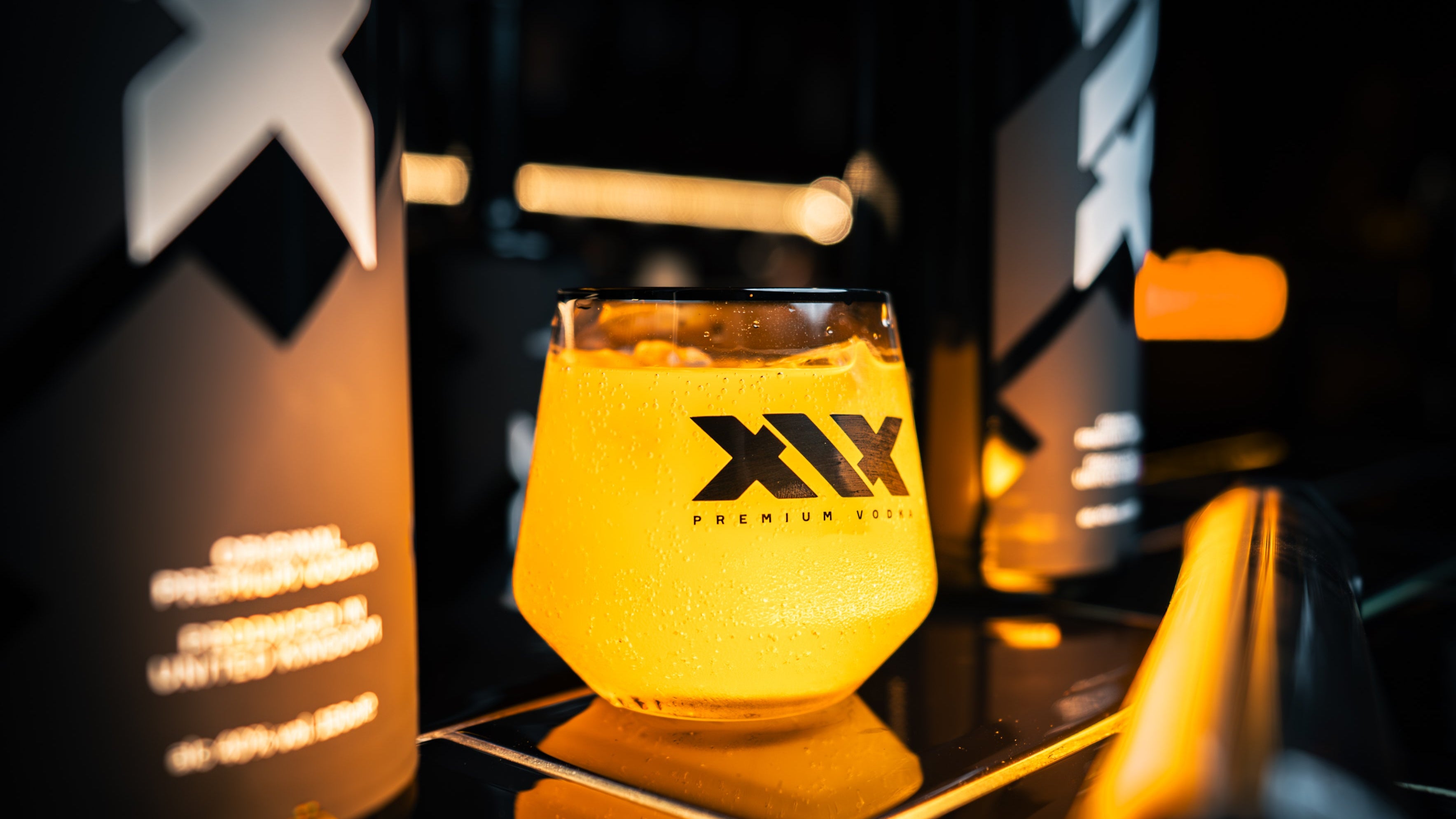 Glass of yellow liquid with XIX logo on a dark background